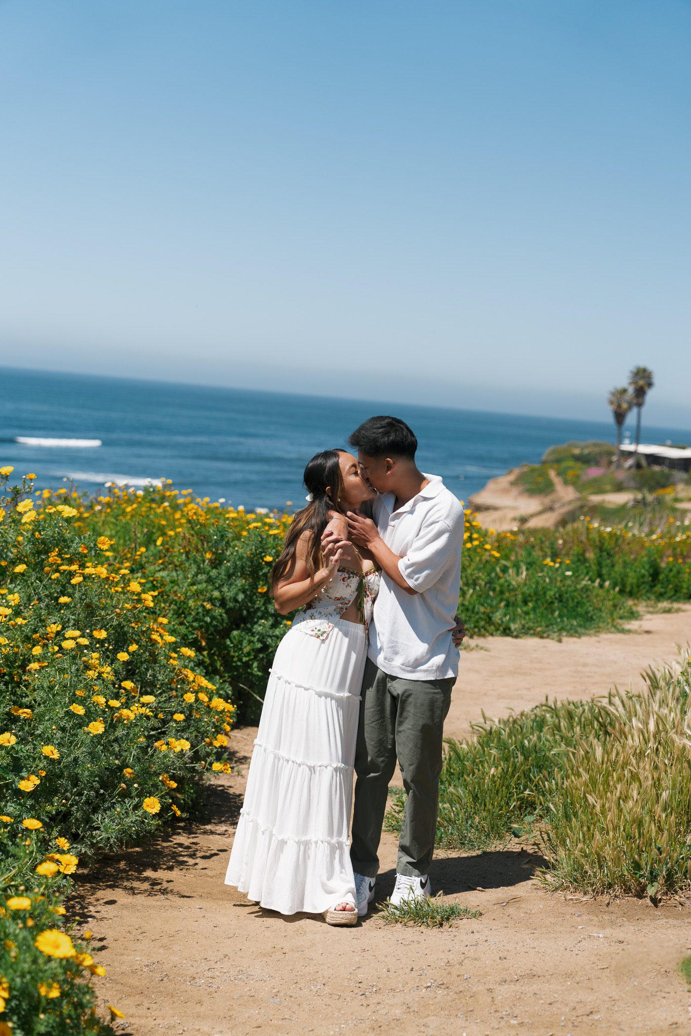 a couple kissing with wildflowers and the ocean in the background.