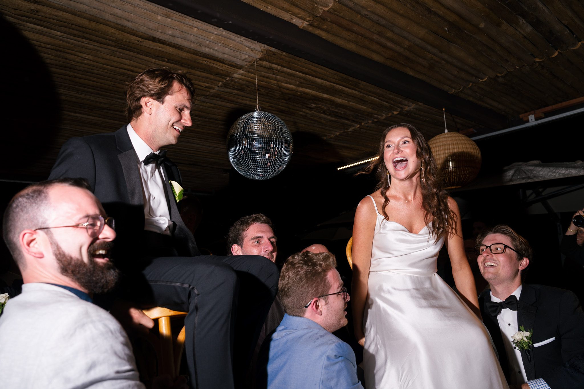 newlyweds being carried on chairs that the wedding guests are carrying. 