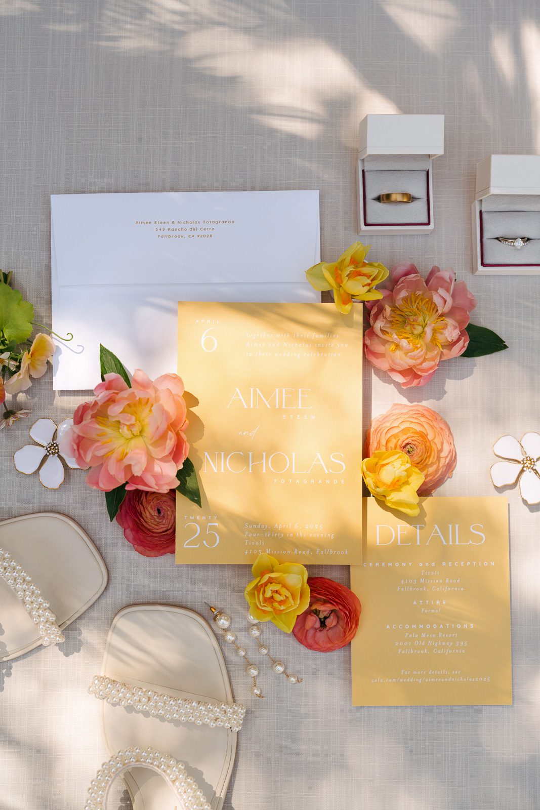 flat lay including the wedding invite, heels, flowers, rings, and earrings. 