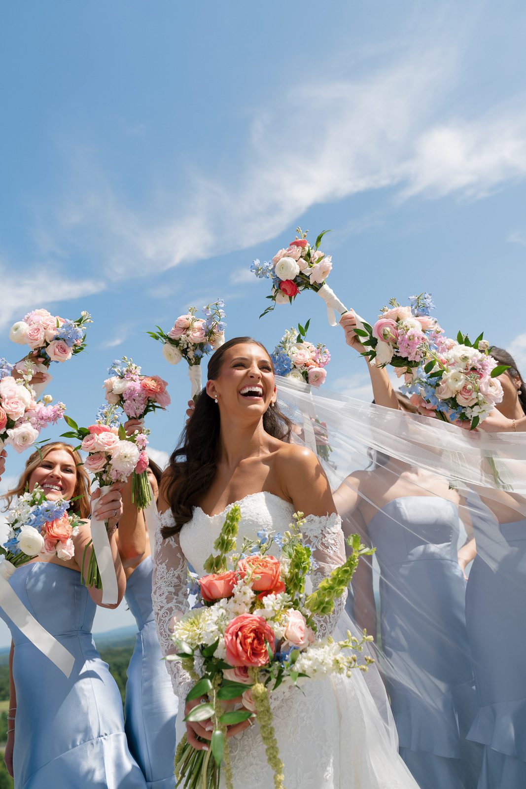 the bride smiling while her bridesmaids hold flowers around her. 