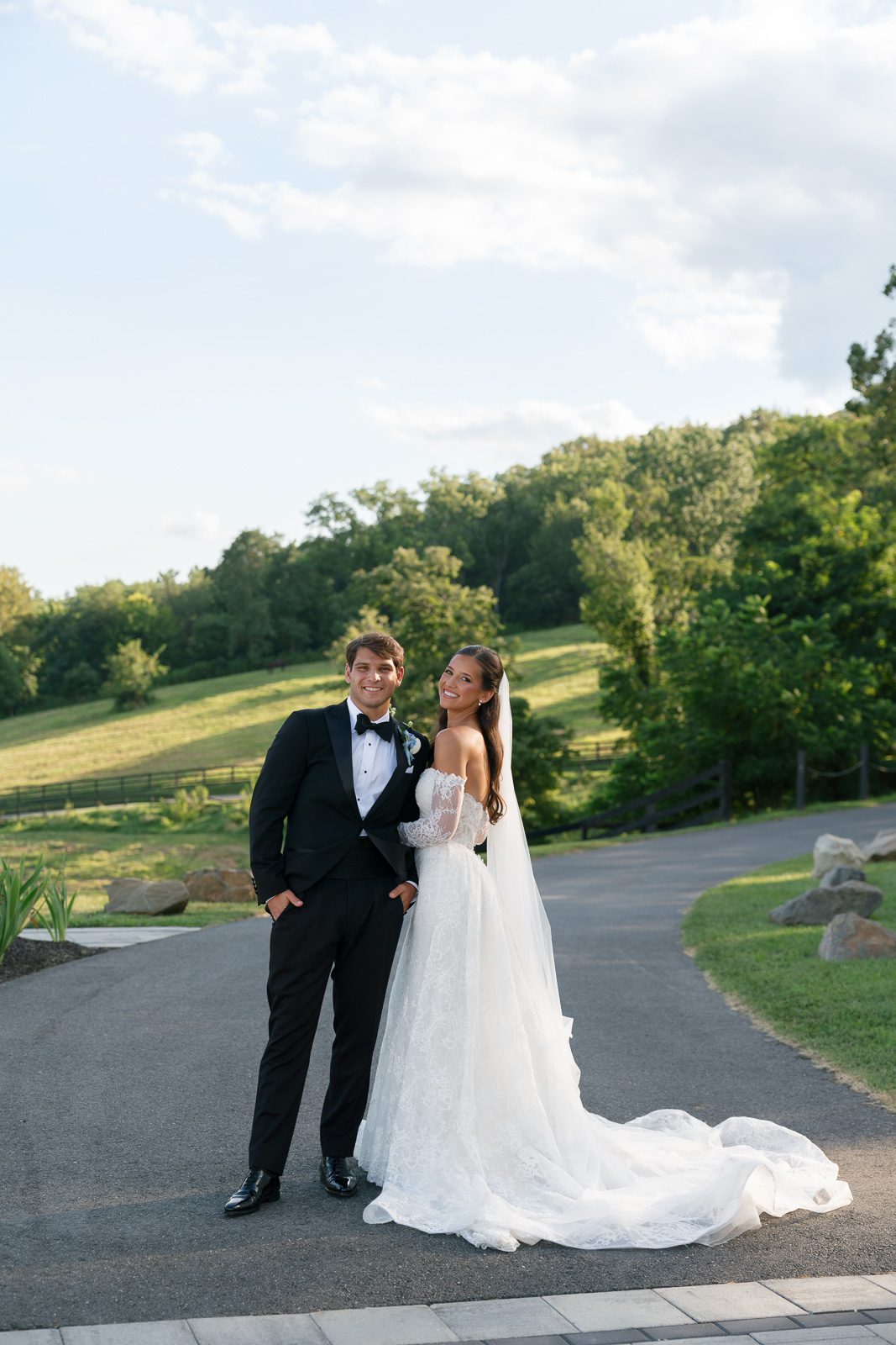 the newlyweds smiling on a country road with trees in the background. 