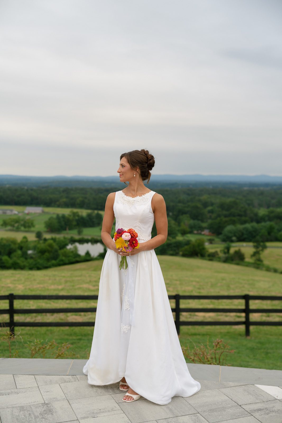 the bride holding a bouquet of flowers looking to her side with tres and mountains in the background. 