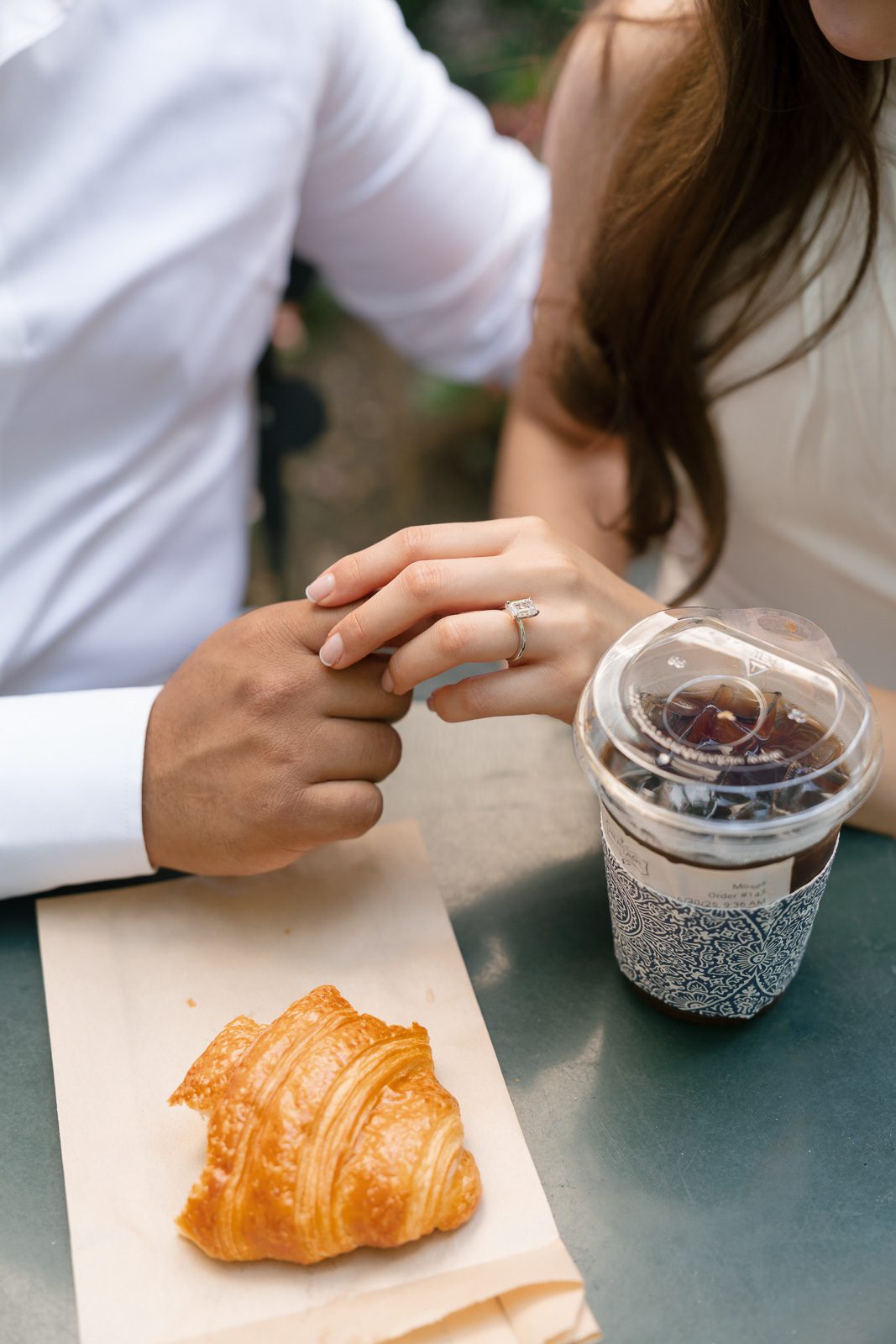 couple holding hands, with a coffee and pastry on the table by them. 