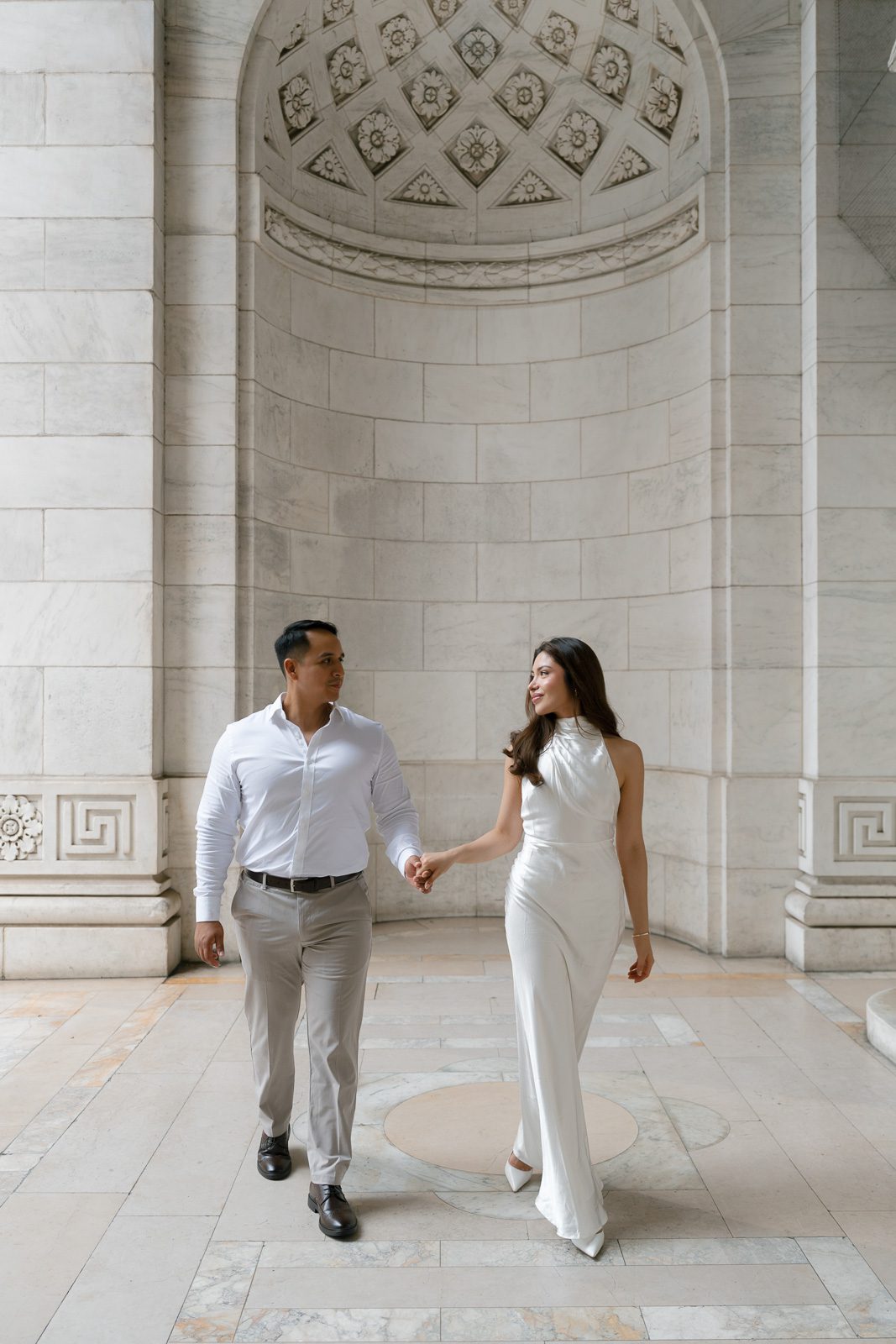 couple holding hand in a new york building filled with marble during their NYC engagement photos. 