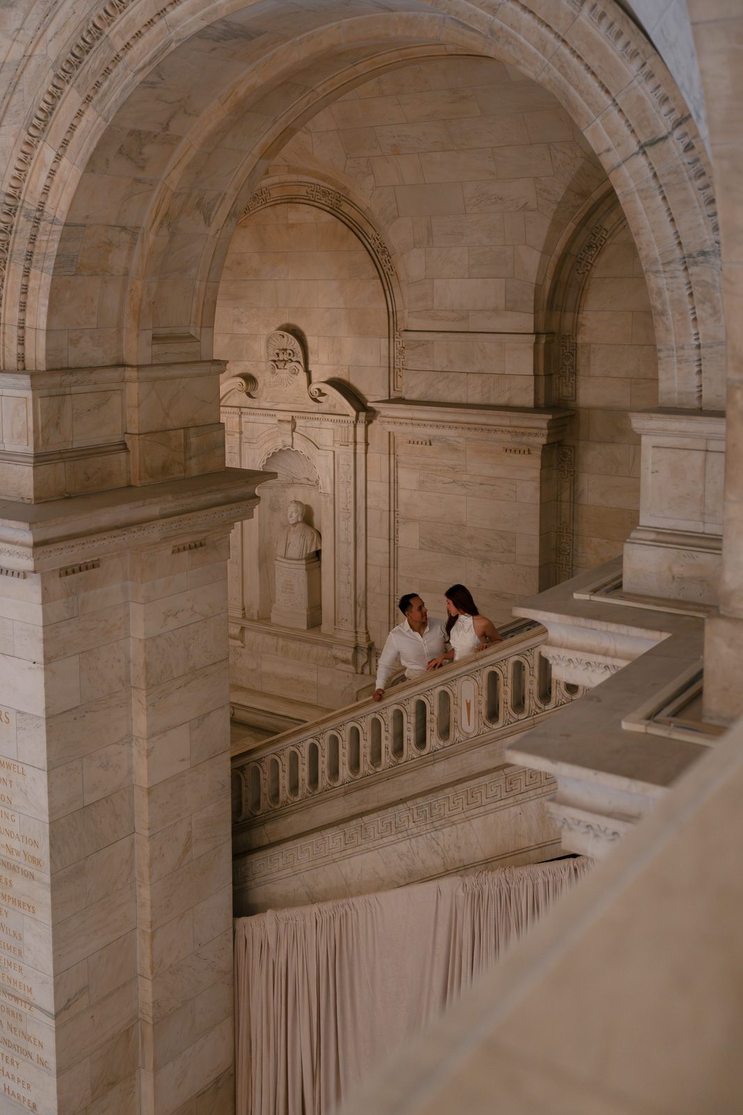 couple walking up an opulent marble staircase during their NYC engagement photos. 