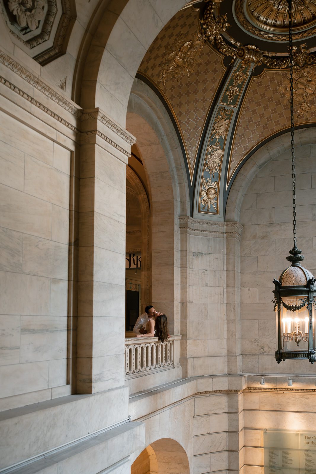 couple leaning against a marble wall, with arches and a lantern around them