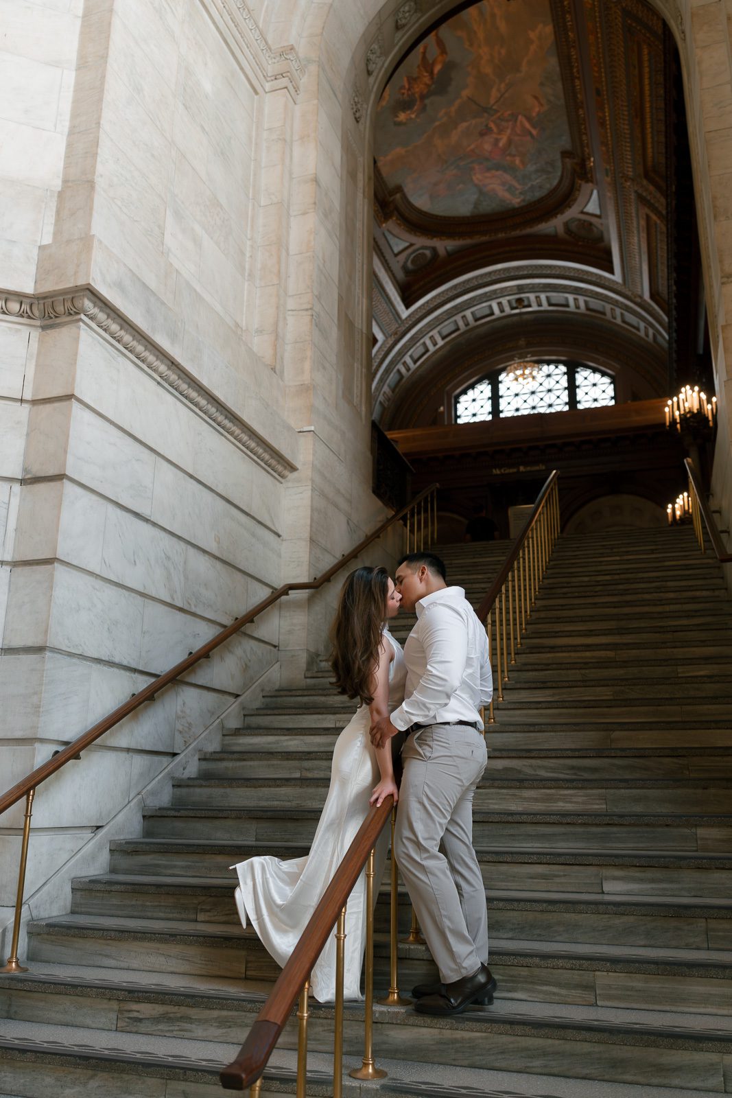 couple kissing in front of a large staircase during their NYC engagement photos. 